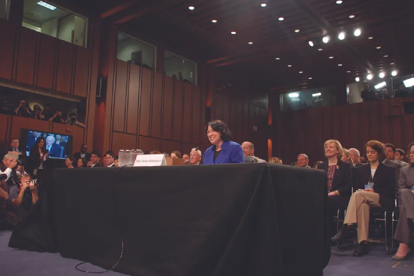 An image of Sonia Sotomayor standing behind a table with a group of people seated behind.