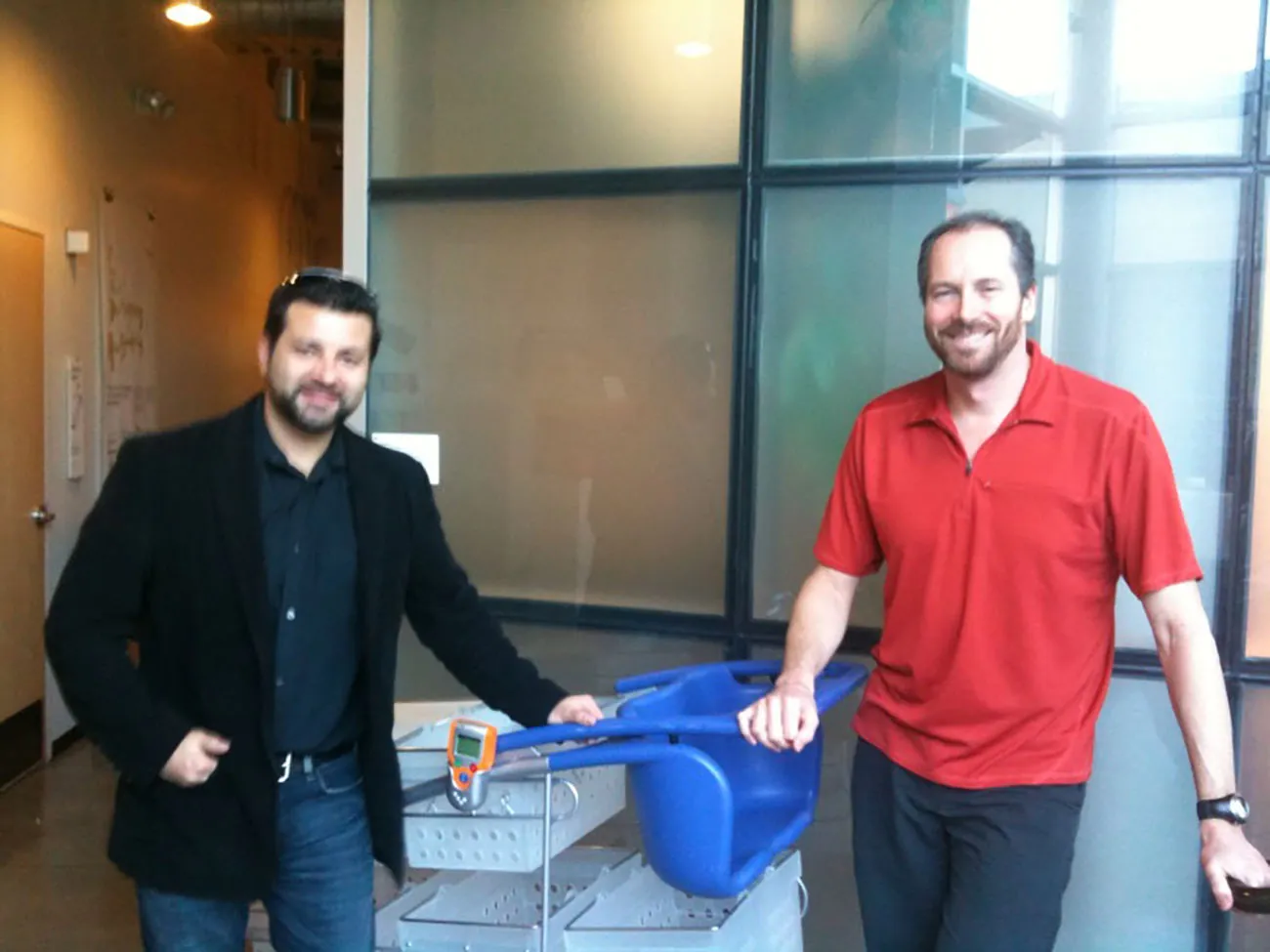 A photo shows two IDEO male representatives posing for the camera with a model of the new shopping cart introduced by IDEO.