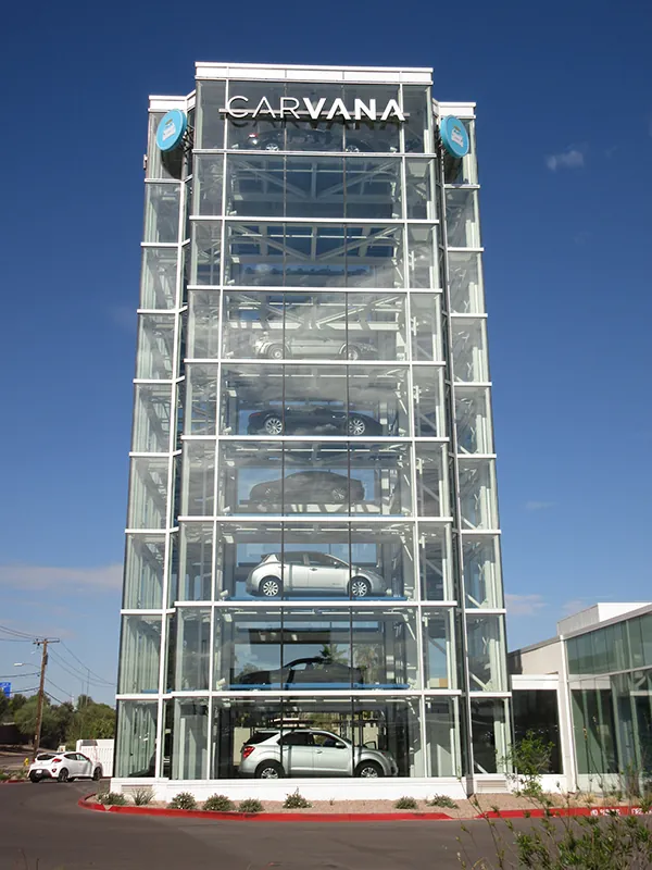 A tall Carvana building is made of glass. Through the glass, you can see a car on each floor of the building. The word Carvana is at the top of the building.