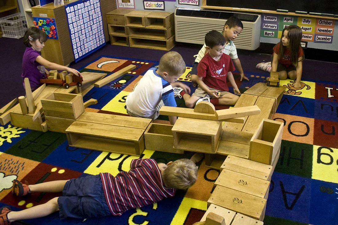 Several children play with wooden blocks and boxes on an alphabet rug.