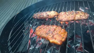 A photograph of meat being cooked on a charcoal grill.