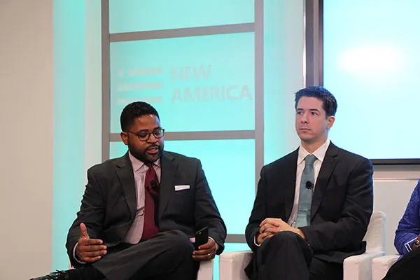 American print and television journalist and commentator on politics, Jamil Smith, takes part in a panel discussion. Two other participants are seated nearby.