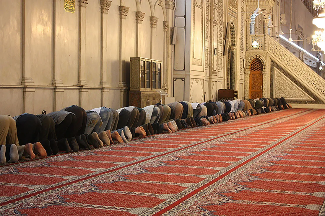 Several dozen people are positioned on their knees with their heads down, inside a mosque.