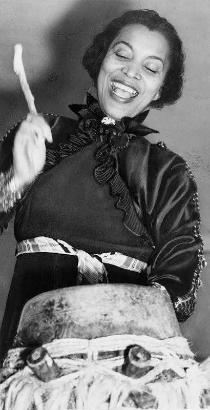Zora Neale Hurston smiling and playing a drum.