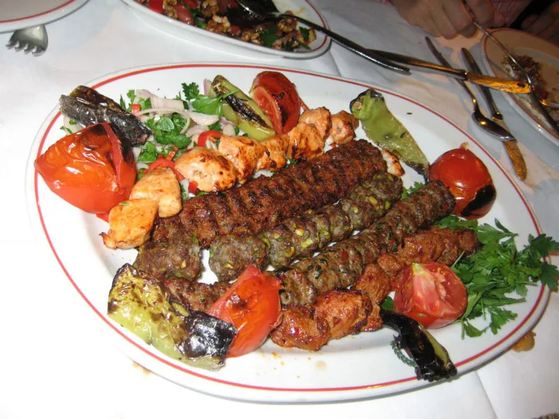 A plate of chicken and beef kabobs surrounded by roasted tomatoes and peppers.