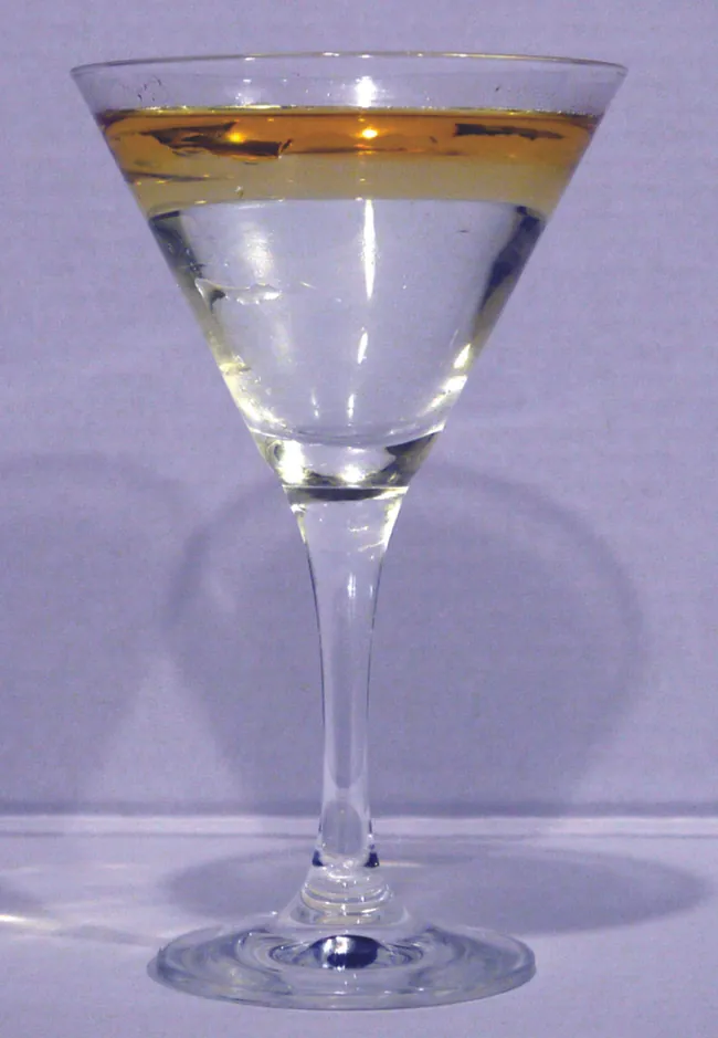 Esta es una foto de una copa de martini transparente e incolora que contiene una capa de líquido de color dorado que descansa sobre un líquido transparente e incoloro.