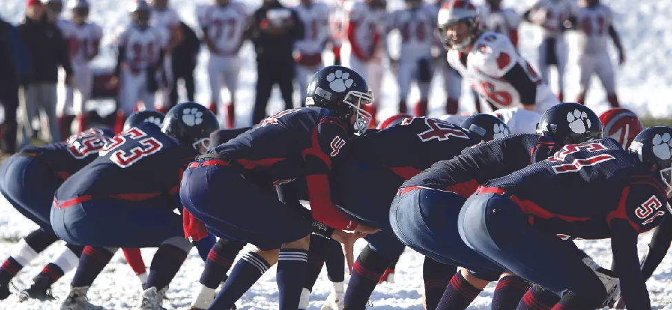 A photo of American football players lining up on the line of scrimmage.