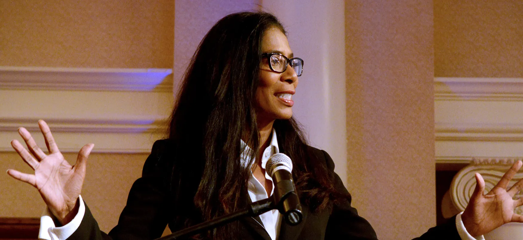 A female in business attire stands at a microphone and speaks.