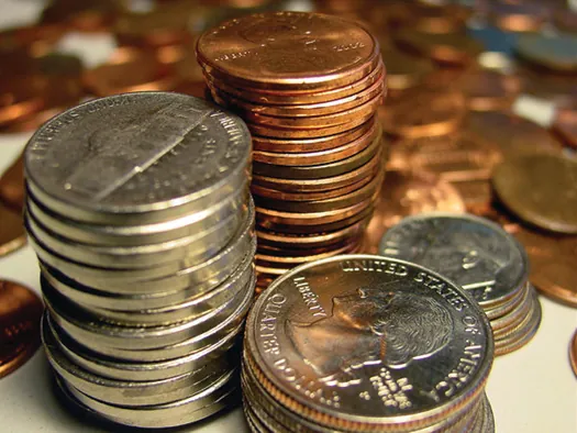 An image of a large stack of pennies, a large stack of nickels, a shorter stack of dimes, and a stack of quarters is shown. There are several coins in the background.