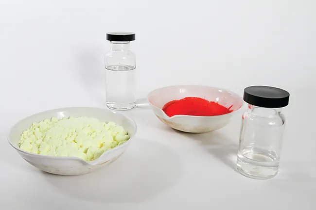 Esta foto muestra dos viales llenos de un líquido incoloro. También muestra dos cuencos: uno lleno de un polvo blanquecino y otro lleno de un polvo rojo brillante.