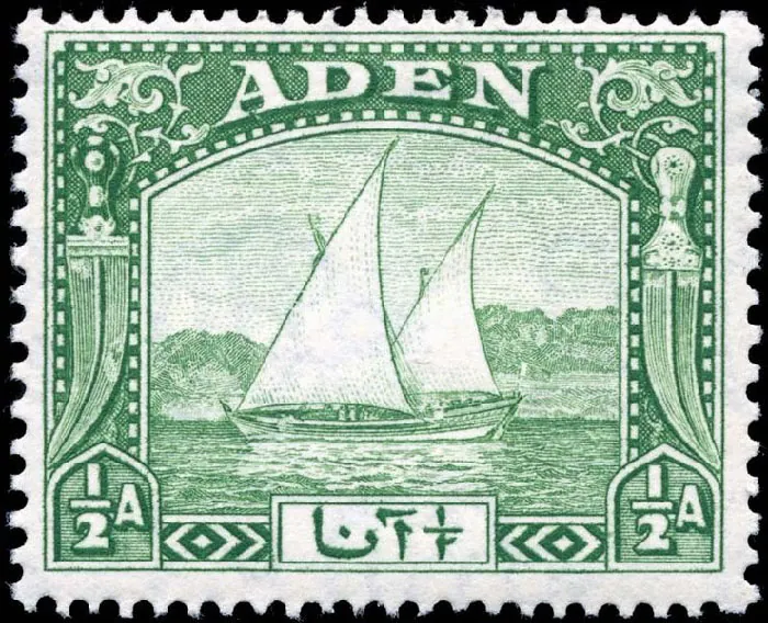The postage stamp is white and green with a black border. The middle of the stamp shows a sailing ship with two masts in water with trees in the background. An ornate knife is drawn on both sides of the stamp, with vines above each. Across the top is the word “Aden” and “1/2A” is in each of the bottom corners.