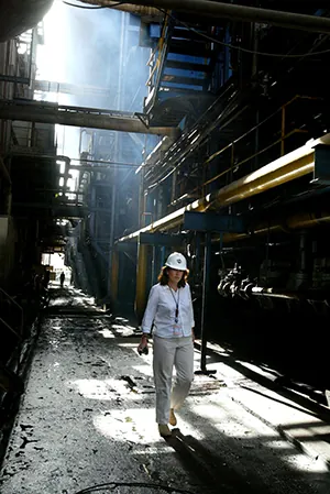 A woman wearing a hardhat walks between steaming pipes.