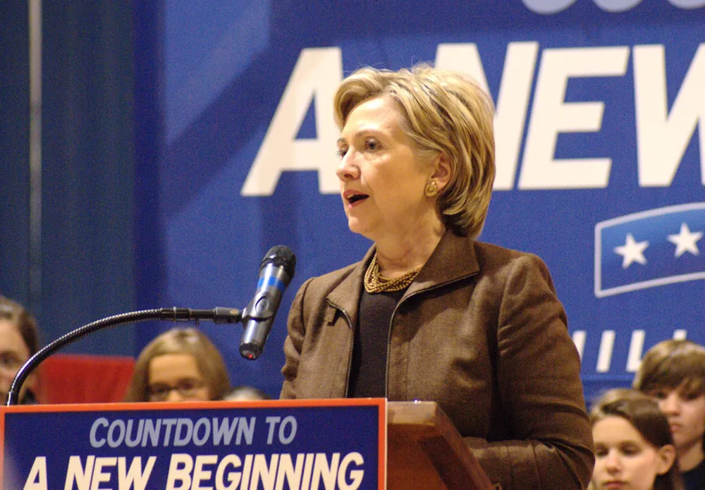 Then-presidential candidate Hillary Clinton is shown standing behind a podium with a placard stating: Countdown to a New Beginning. A number of children are shown in the background.