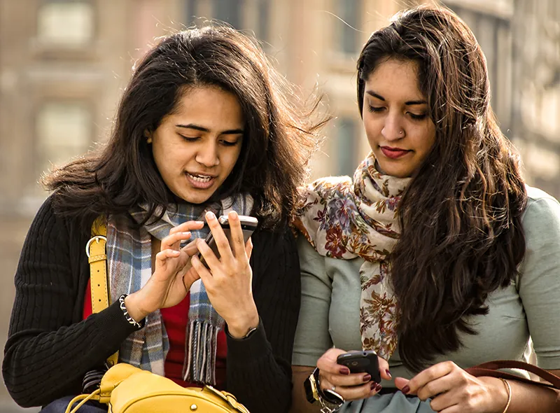 A photo shows two young women using mobile phones.