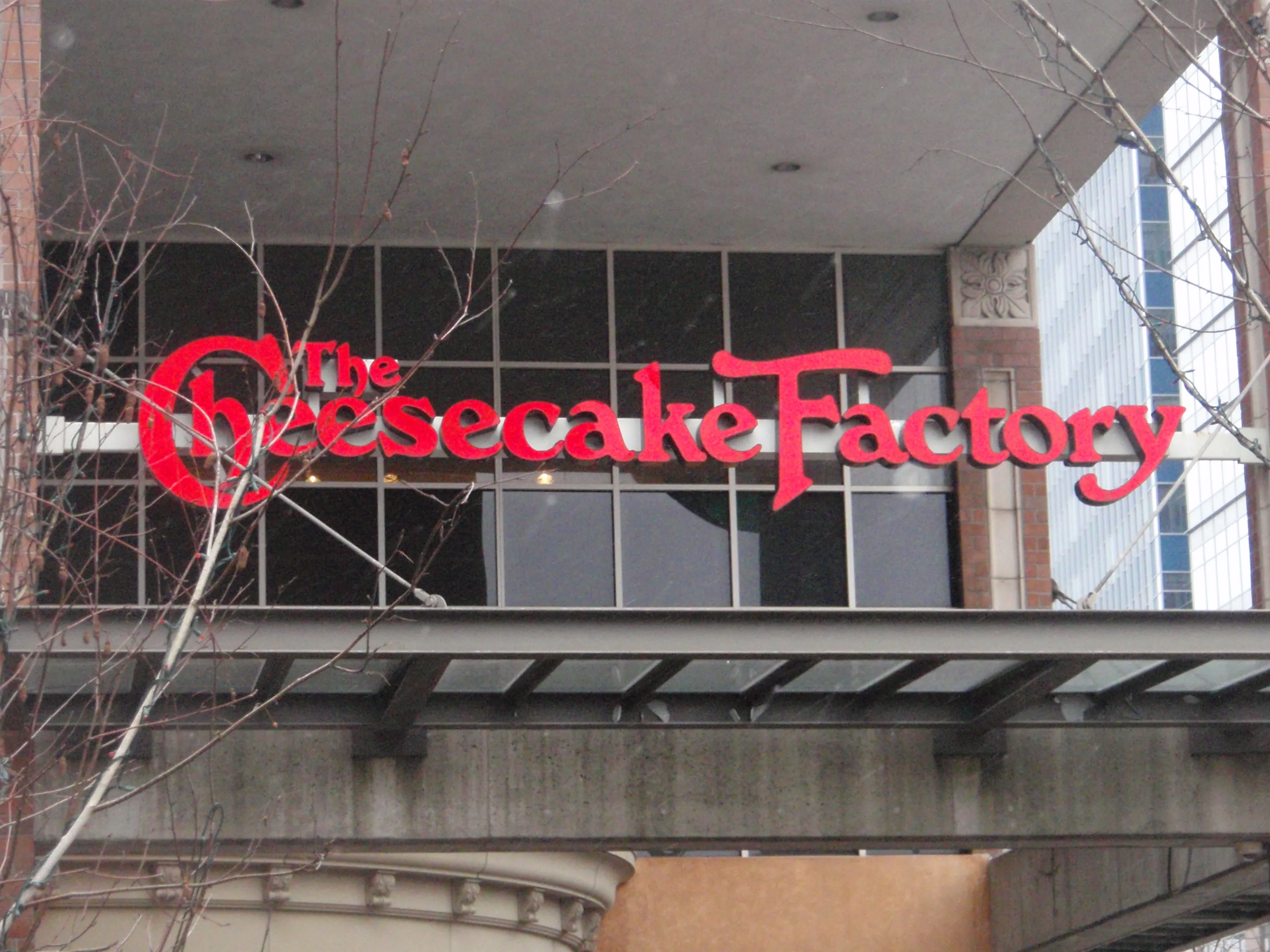 A photograph shows a large Cheesecake Factory sign hanging above the entryway of a building.