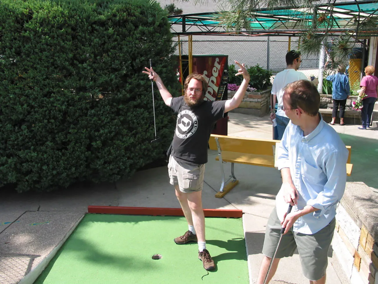 A photo shows a man in casual attire celebrating a hole in one on a miniature golf course, with an untied shoe.