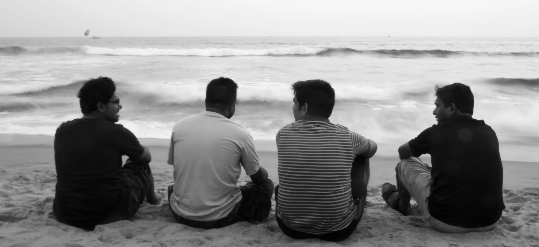 Four young people sit on the beach, engaged in conversation.