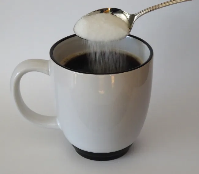 Se muestra una imagen en la que se vierte azúcar de una cuchara a una taza.