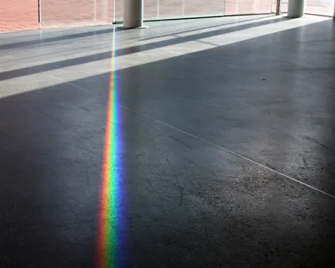 A photo of a rainbow colored beam of light stretching across the floor.