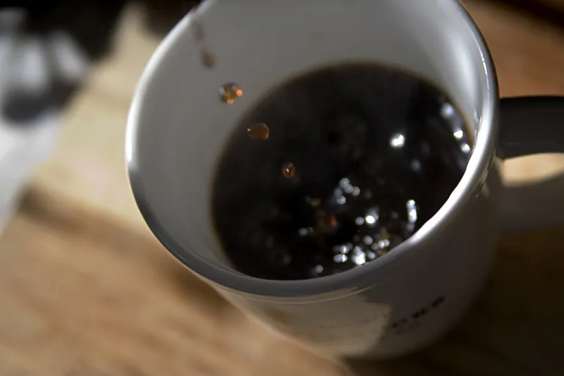 A photo shows a mug half filled with coffee. A few drops of coffee are going into the mug.