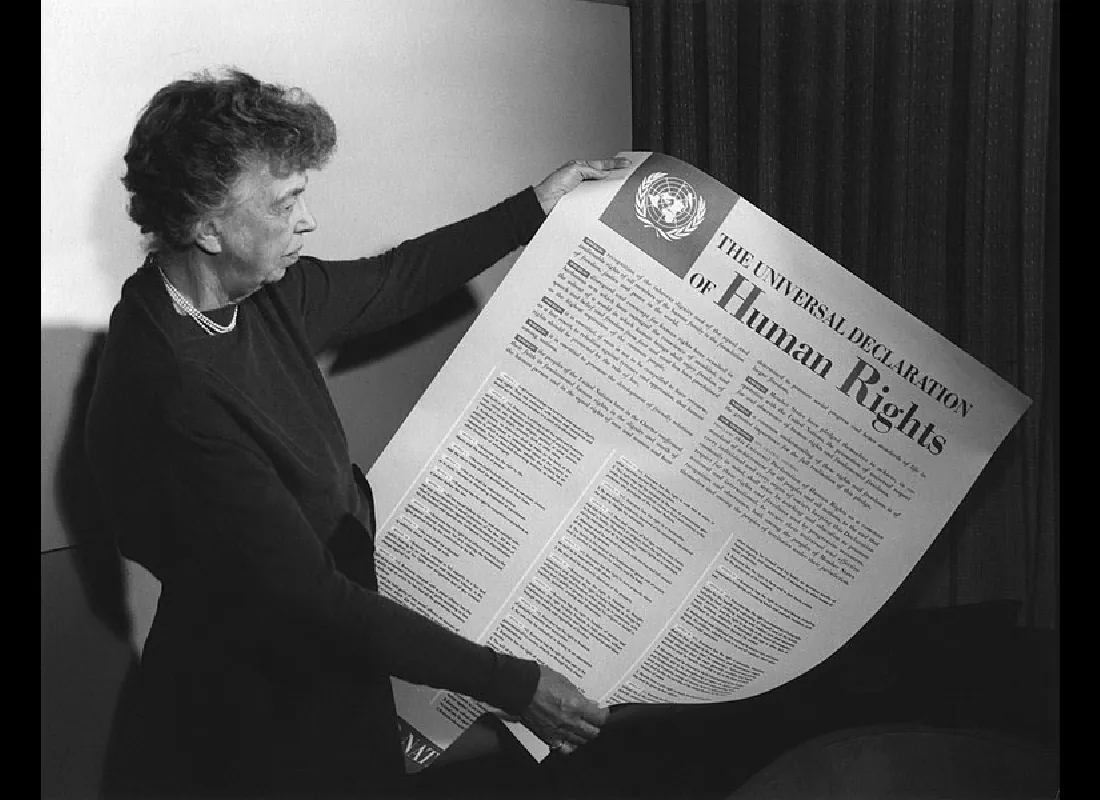 This photograph shows Eleanor Roosevelt holding a large document titled “The Universal Declaration of Human Rights.” The logo for the United Nations is in the upper left corner of the document.