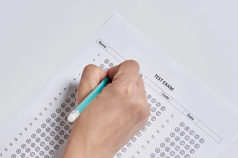 A hand is holding a pencil and filling in the scantron sheet.