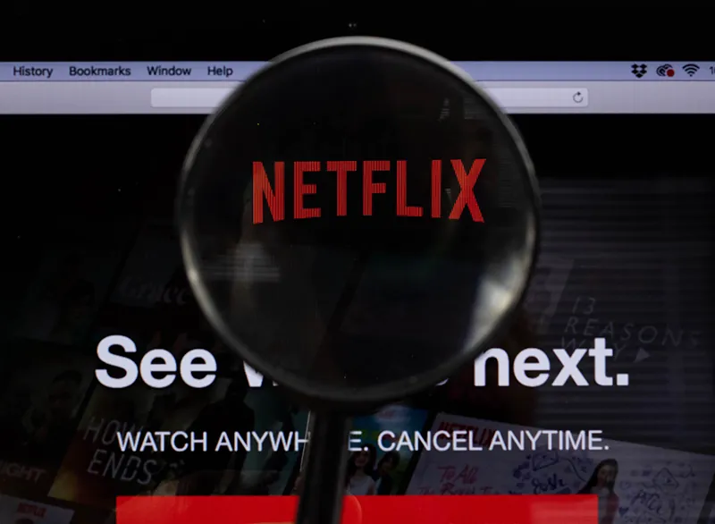 A screenshot of a Netflix ad. A magnifying glass is held over the word Netflix. Underneath it says See what’s next. Watch anywhere. Cancel anytime.