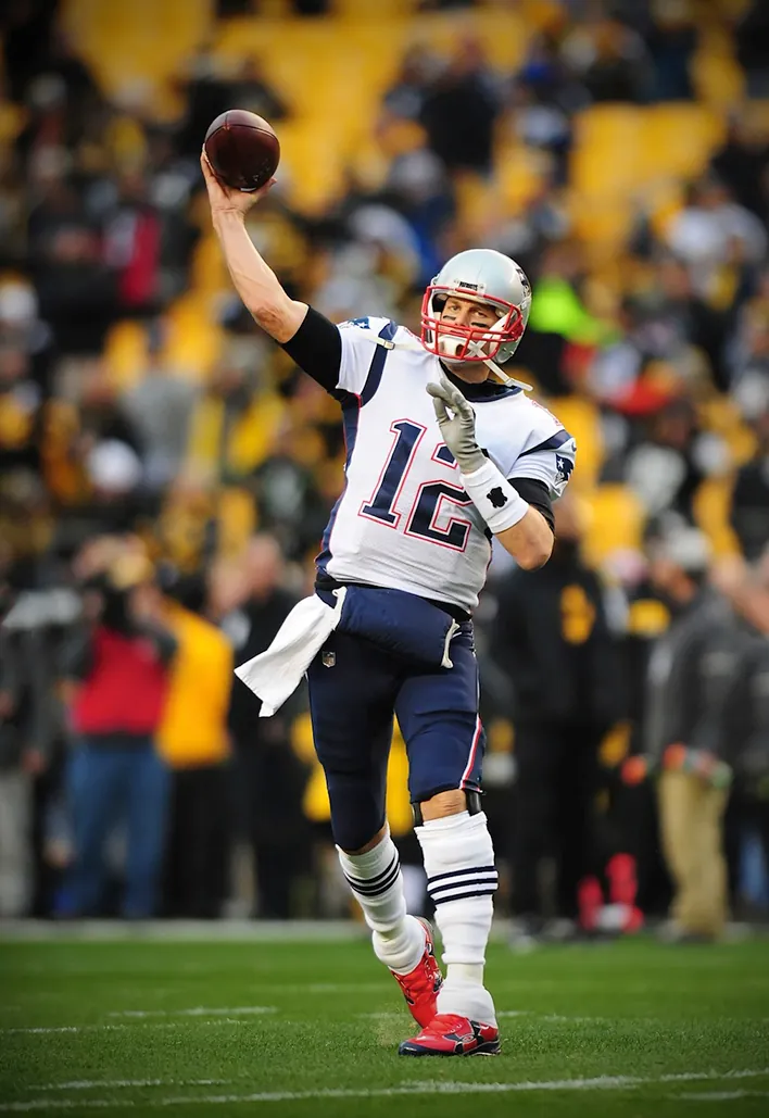 A photograph of Tom Brady in a field throwing a pass.