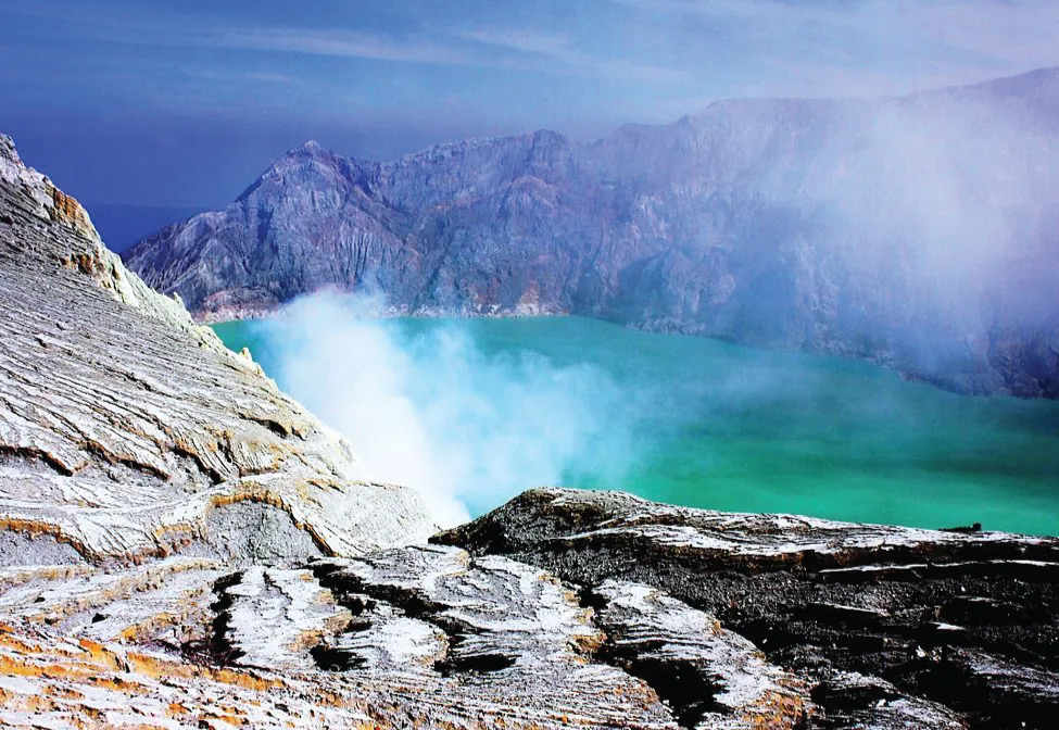 Se muestra un lago rodeado de picos rocosos y montañosos. Un vapor blanco se eleva desde el suelo cerca del lago.
