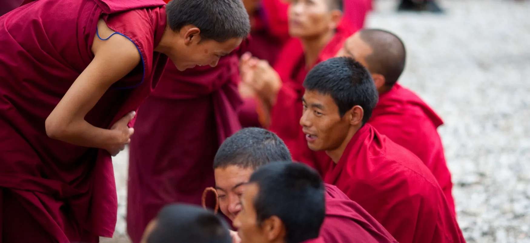 Buddhist monk in red garment bends to speak with other monks in red garments.