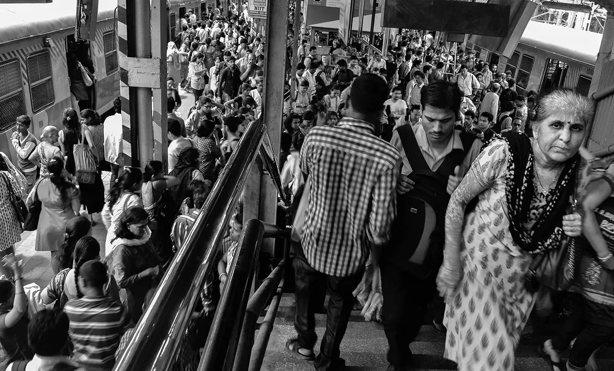 A group of people ascends and descends stairs in a very busy, crowded train station.