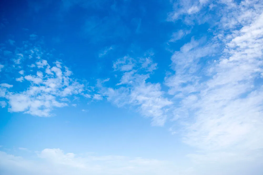 A photo shows a blue sky with light scattered clouds.