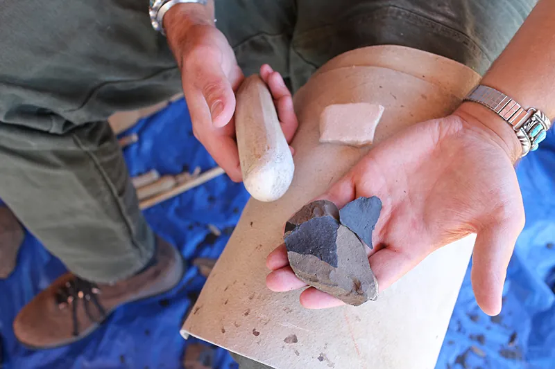 Close up view of two human hands. One hand holds a bone or antler tool, while the other is open with a split piece of flint in the palm.