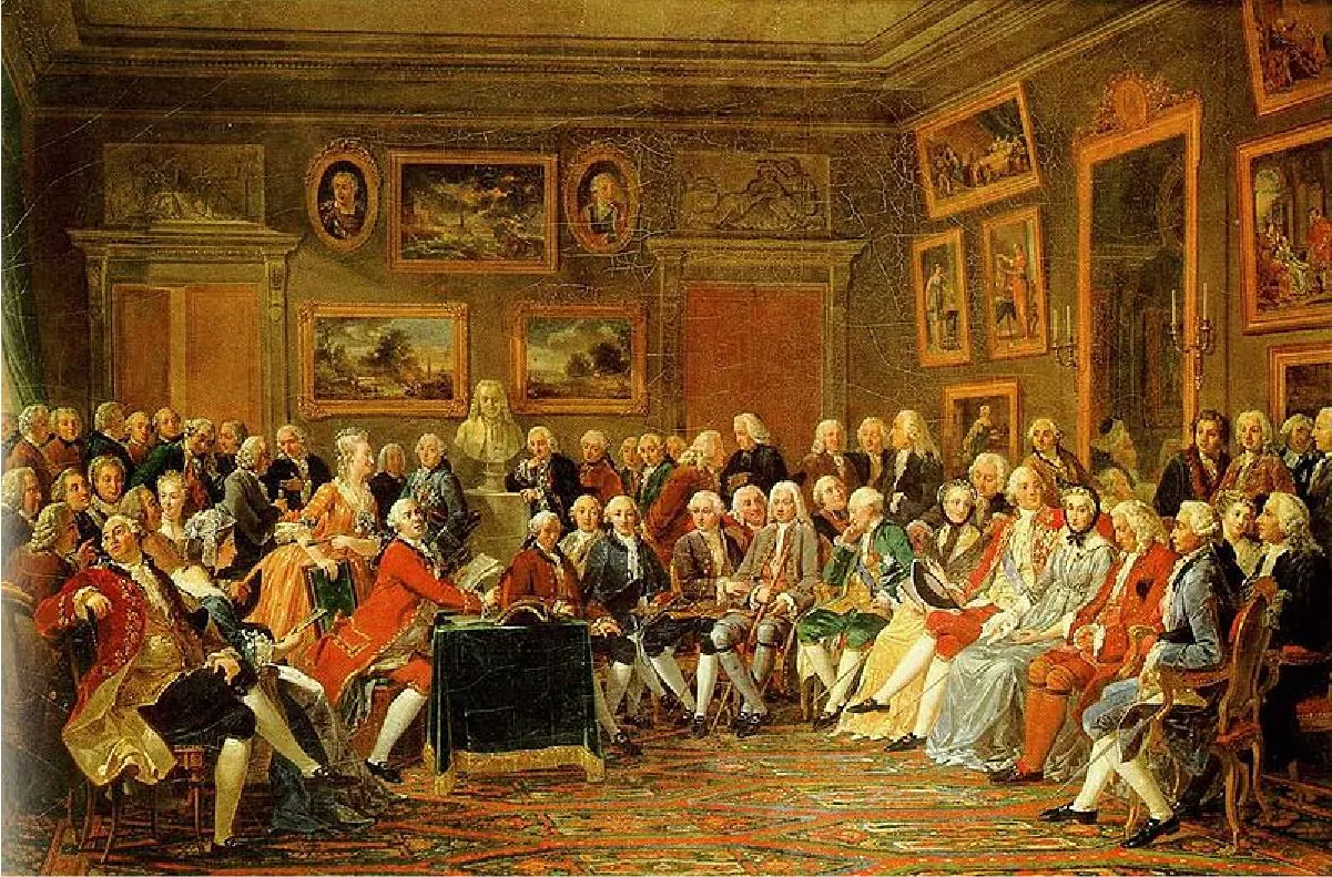 A crowd of people sit around a richly decorated room. There are multiple paintings on the walls and a colorful carpet. The men are all dressed in knee breeches and ornate coats. The women all wear long dresses.