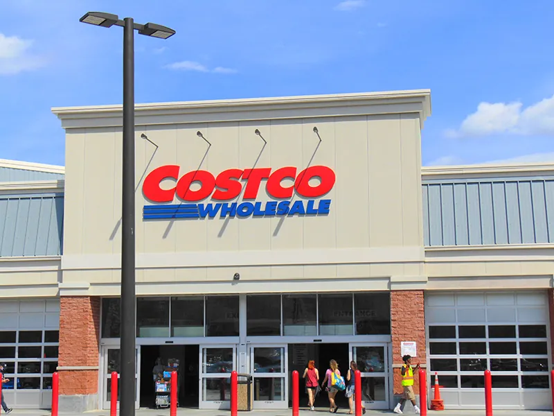 Costco Wholesale is written on the storefront above the doors; people are walking in and out of the doors.