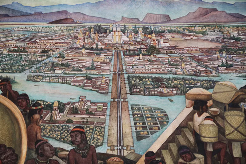 A painting of a complex city built onto an island. Several Aztec people are in the foreground, some carrying burdens on their heads, and a long straight road leads to a triangular-shaped temple in the back of the image.