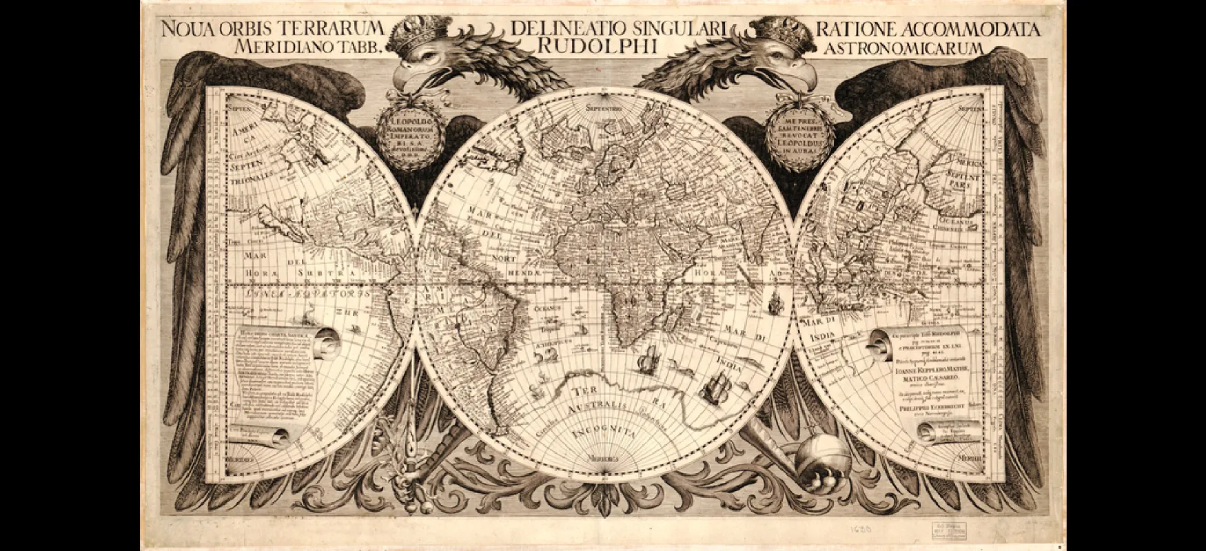 This image shows a map of the world. The map is made up of a circle in the middle and two semicircles on either side. The margins around the map are decorated with the Germanic, double-headed imperial eagle. The Latin words “Noua orbis terrarum delineatio singulari ratione accommodata meridiano tabb. Rudolphi astronomicarum” appear above the image.