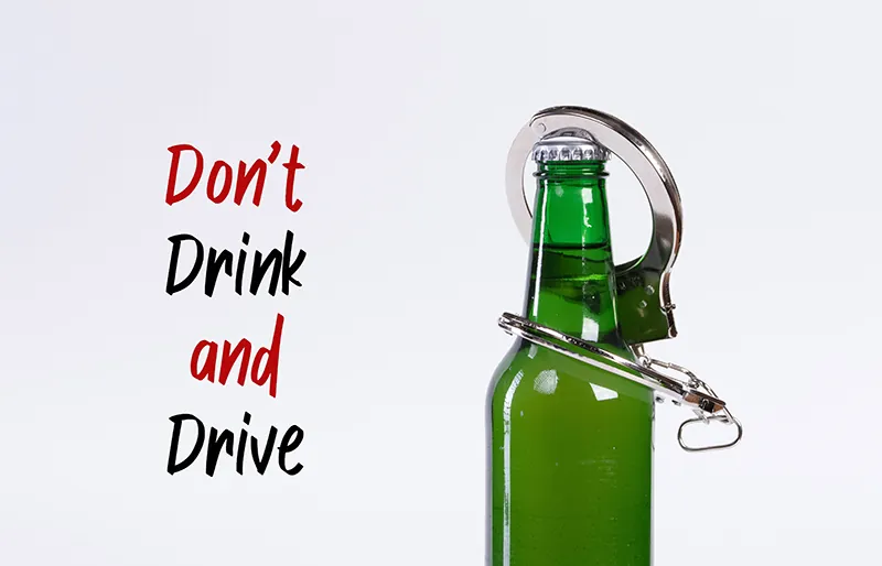 Handcuffs are hung from the neck of a beer bottle with the words don't drink and drive next to the bottle.