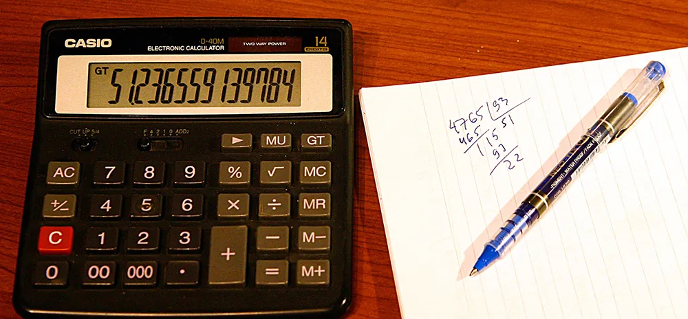 A close-up view of a notebook show a mathematical calculation. A calculator and a pen are placed by the notebook.