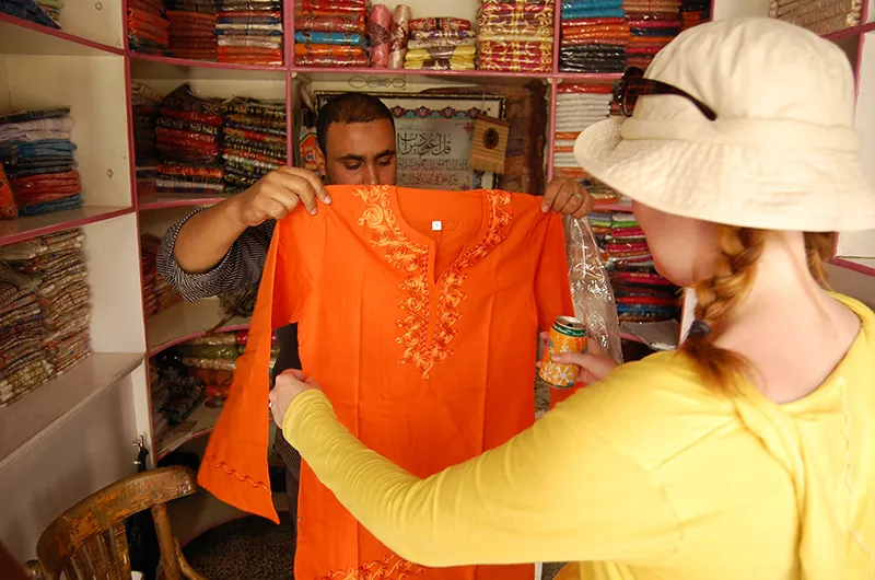 A shopkeeper displays an orange shirt to a customer, who examines it.