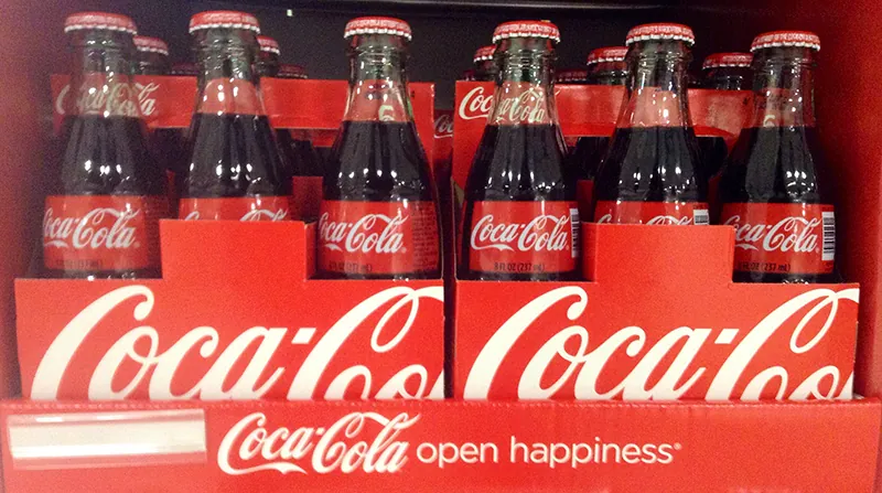 Two six packs of coca cola bottles are shown in a display. The words “Coca Cola open happiness” are written at the bottom of the display.