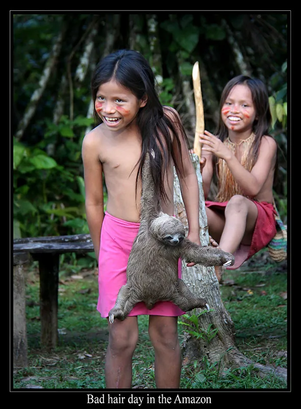 Two smiling children with long black hair and painted faces. A sloth dangles from the shoulder of one of the children.
