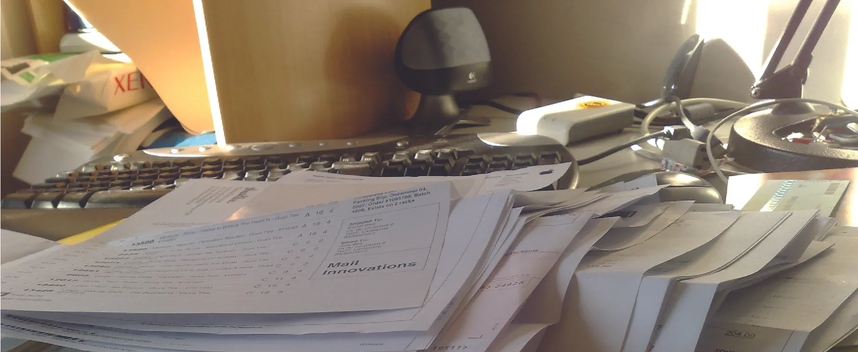 A photograph of a messy desk piled with papers, a computer keyboard in the background.