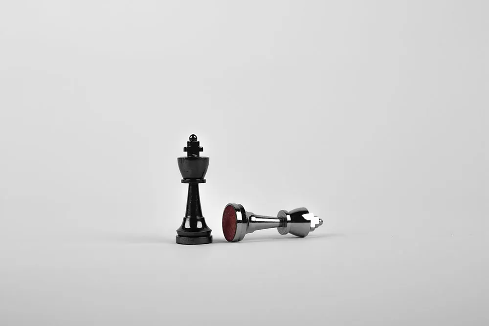 One chess piece stands upright next to another that lies on its side.