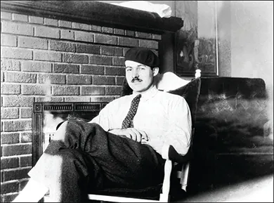 A photograph shows Ernest Hemingway reclining in a chair in front of a fireplace.