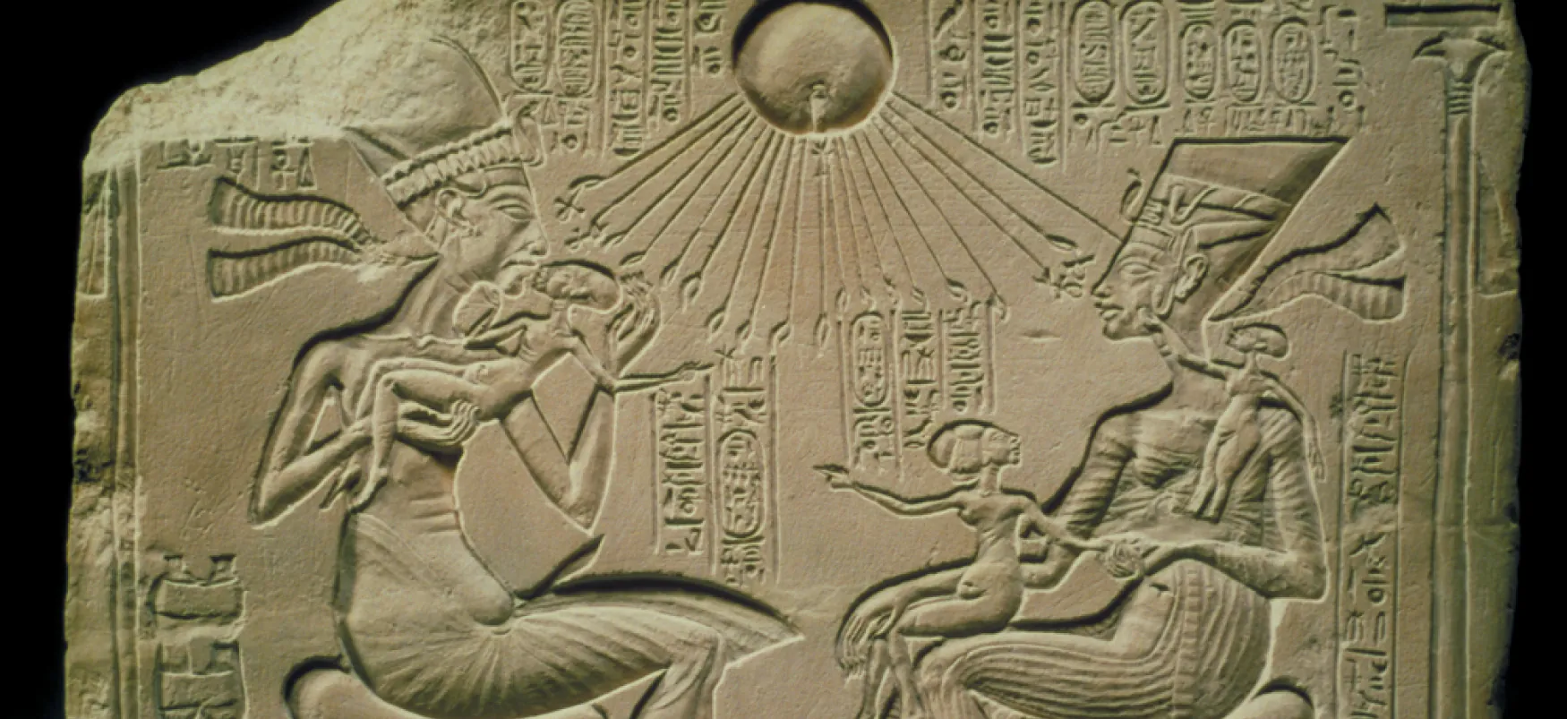 Stone fragment carved with images of two adults holding children. Above them is the sun, with rays reaching down to touch the adults and the children. Egyptian hieroglyphs surround the images.
