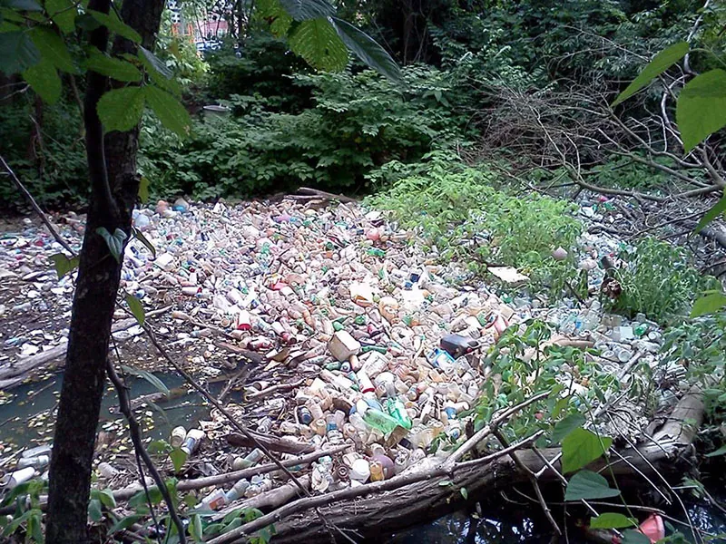 Thousands of bottles and other containers and garbage float in a large mass in a river.