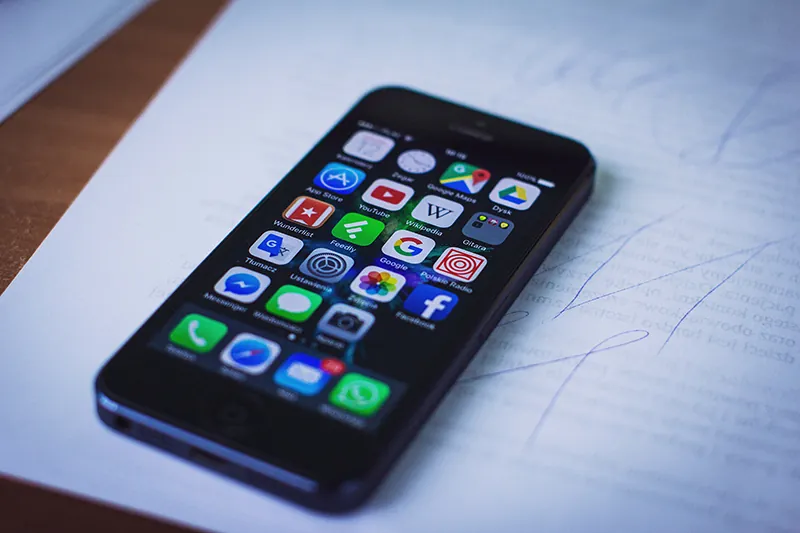 A smartphone with apps displayed on its home screen is on a pad of paper on a table.