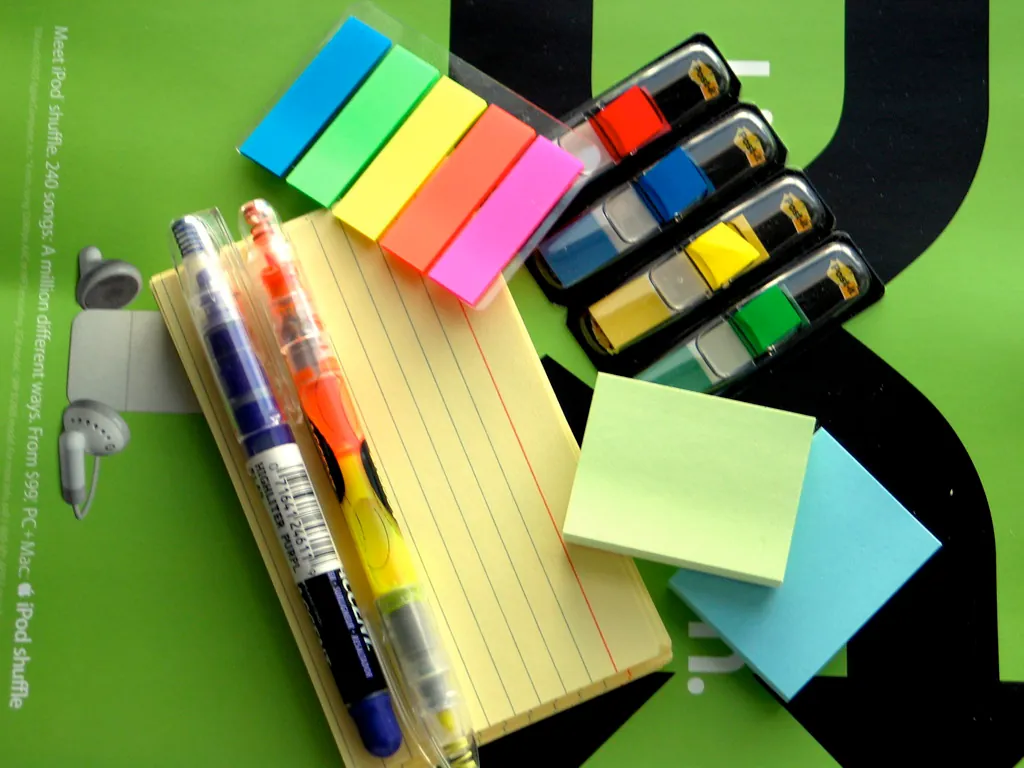 A photo shot directly from the above shows a set of stationery items including, papers, highlighters, pens, and sticky labels.