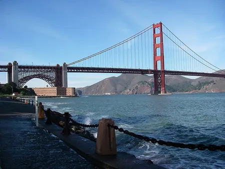 A picture of the Golden Gate Bridge, which includes cables that drop from tall towers. The picture also includes a walkway barrier consisting of chains hung between vertical structures.